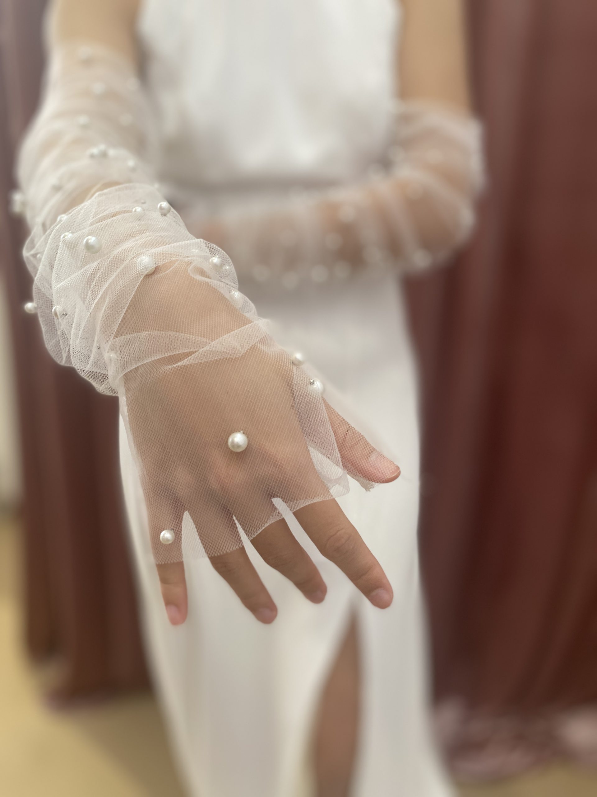 Ein Model zeigt seine Hand, die in einem Handschuh zum Brautkleid steckt.